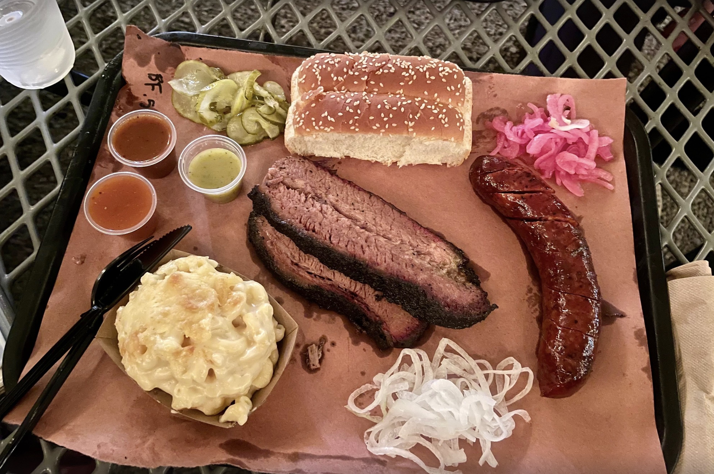 Lewis barbecue tray with sausage, brisket, mac and cheese, pickles, bread and some sauces. 